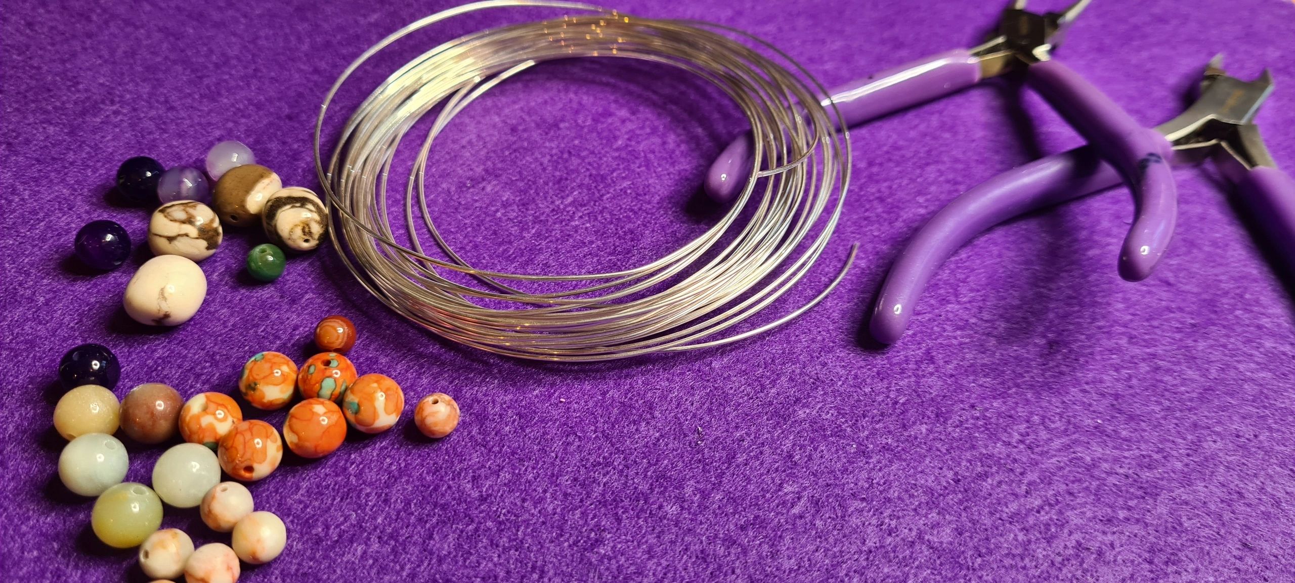 Jewellery making materials, wire, beads and tools on a purple work surface.